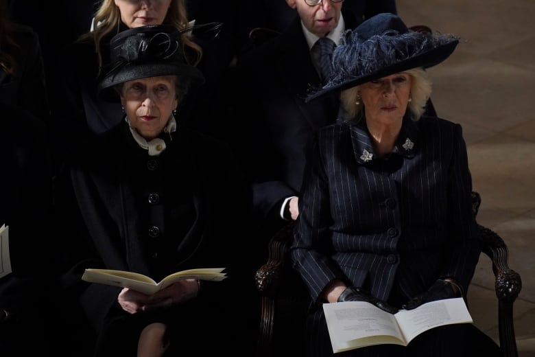 Two people holding programs sit in chairs in a large church.