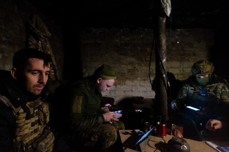 Three soldiers sit in the dark surrounded by various screens. 