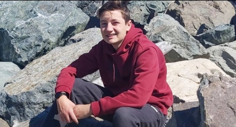 Boy in sweatshirt, sitting on large rocks, smiling at the camera.