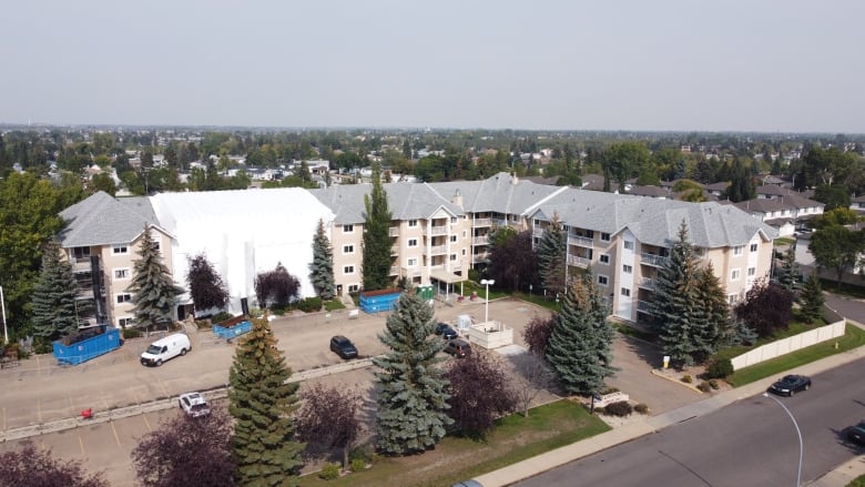 An aerial shot of a large condo building. A white tarp covers one wing of the property. 