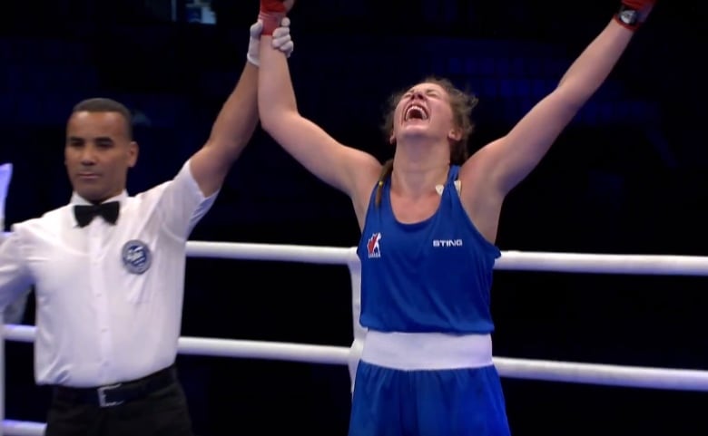 A referee holding up the arm of a girl wearing a blue boxing outfit