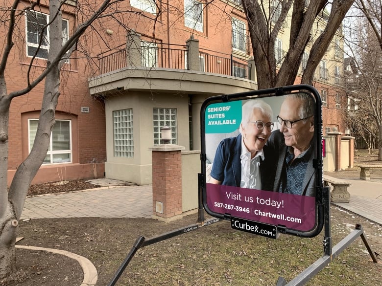 A sign outside a building depicts an older couple laughing and reads, "Seniors' suites available. Visit us today."