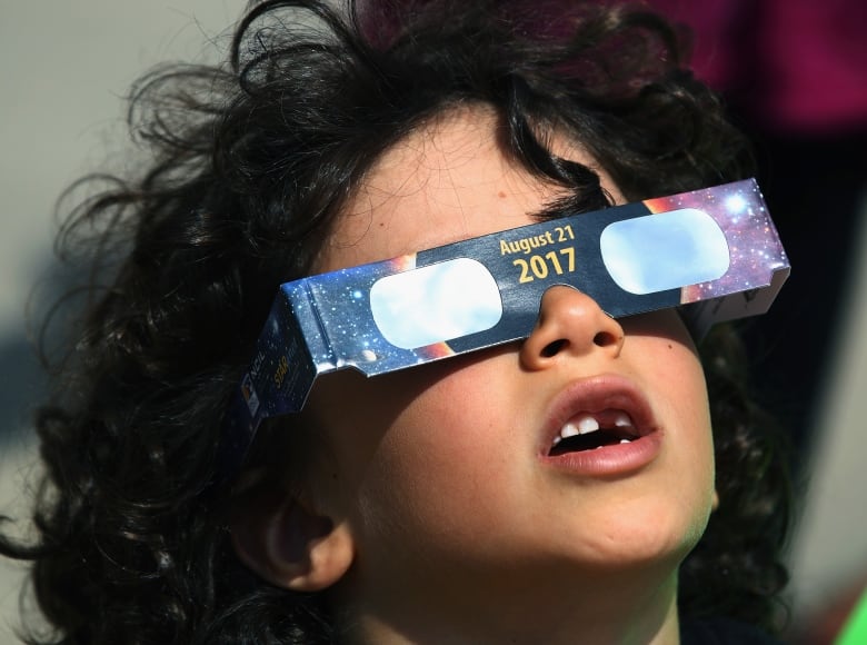 Child wears disposable eclipse-glasses with 2017 written on them and looks skyward.