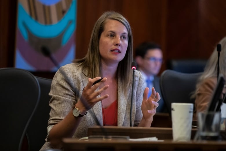 A white woman gestures as she speaks in council.