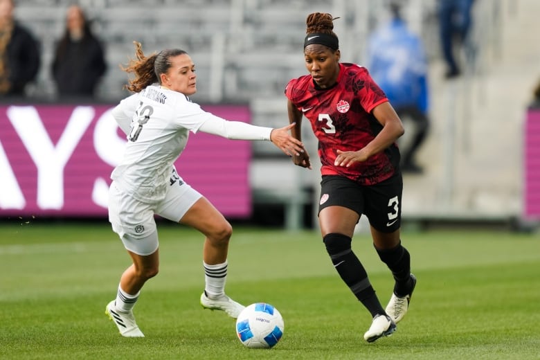 A female soccer player runs with a ball past an opponent.