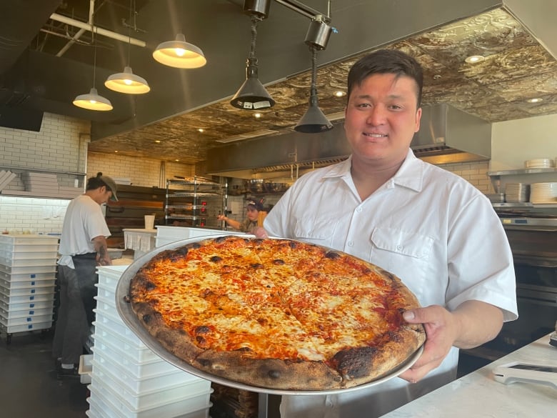 A man holds a large pizza on a pan. 