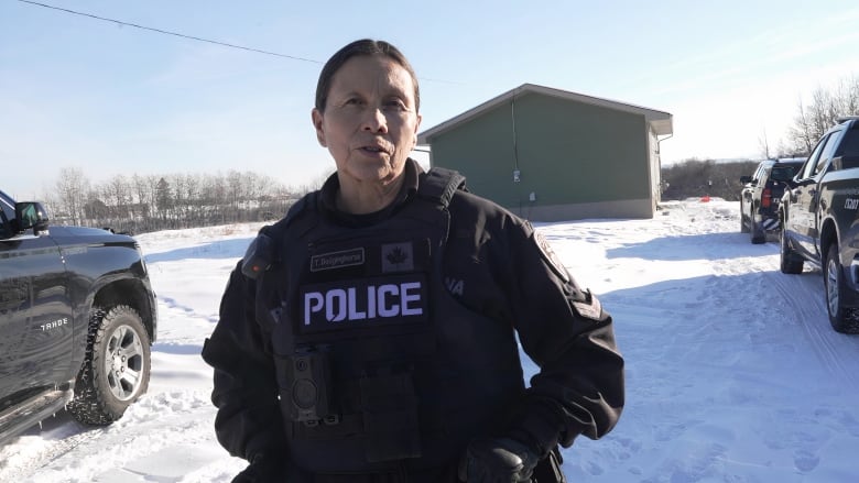 A close-up shot of a woman in a black police uniform. Her hair is tied up and she is surrounded by snow and cars.