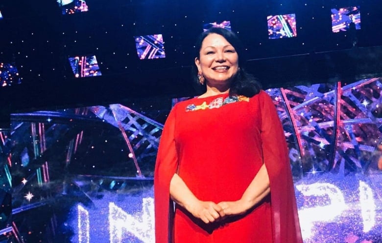 Dawn Madahbee Leach wearing a long red dress, while standing on a brightly lit stage for the Indspire Awards.