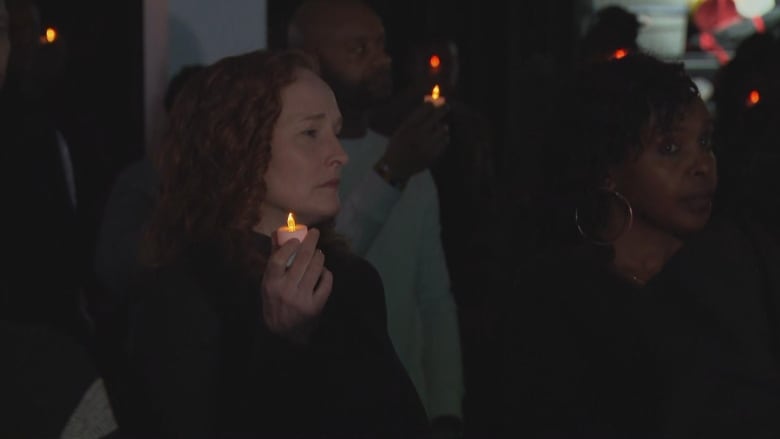 People stand in dark room holding candles.