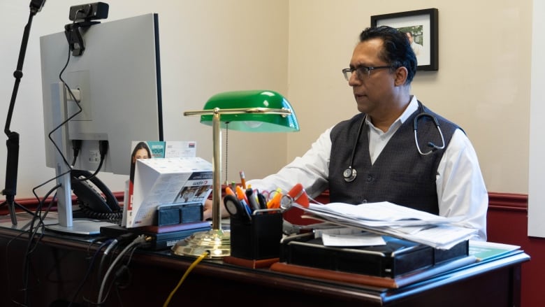 A doctor sits at a computer in his office.