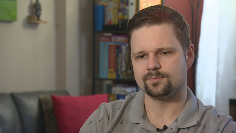 A man in a polo shirt sits in a living room.