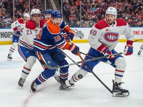 Oilers' Zach Hyman bats at a loose puck in between Canadiens' Kaiden Guhle and Joel Armia, right, at Rogers Place in Edmonton on Tuesday.