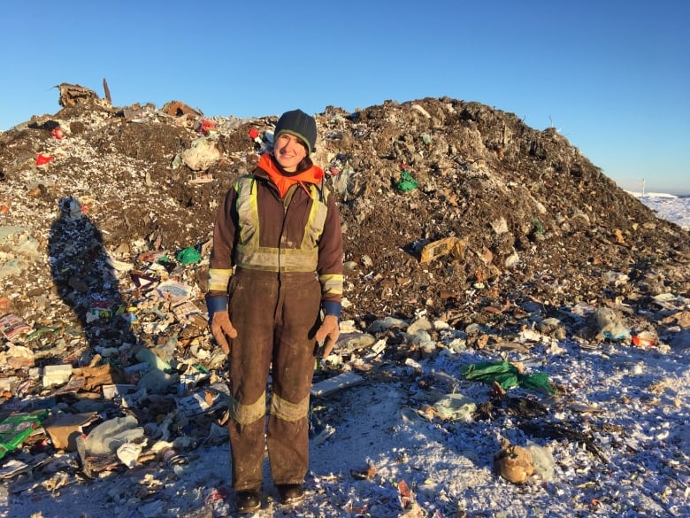 A woman stands beside a pile of stuff.