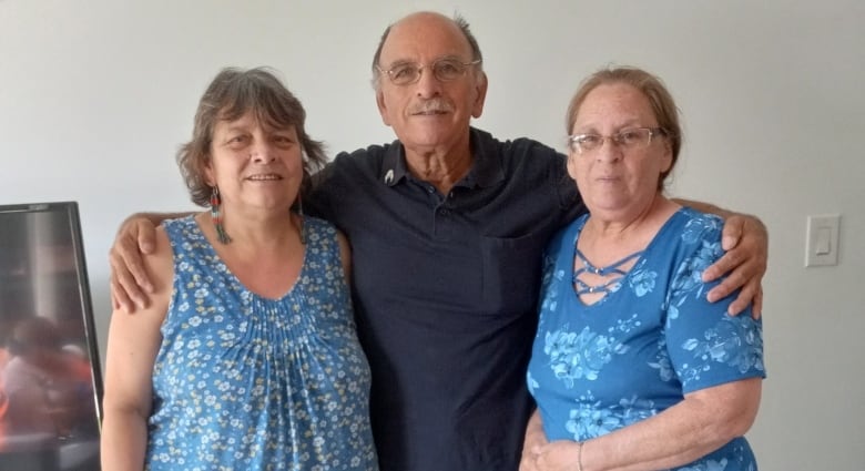 A man is pictured with his arm around two women standing next to him as they face the camera.