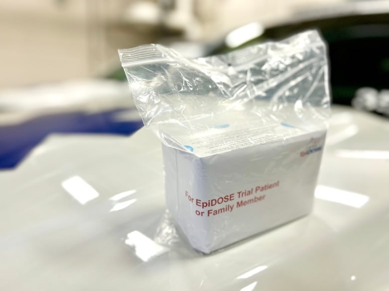 A white container sits in a plastic bag with red lettering that reads: 'For EpiDOSE Trial Patient or Family Member.'