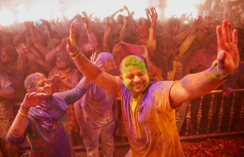 People dance while covered in coloured powder.