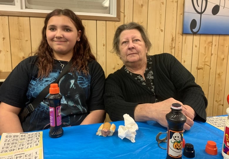 A woman and teen girl at a table with some bingo cards and markers.