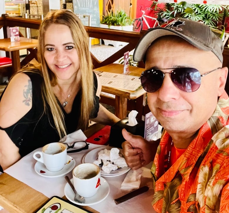 A man and a woman smile while seated at a cafe table.