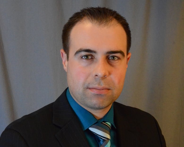 A man in a dark suit, blue shirt and striped tie poses for a portrait.