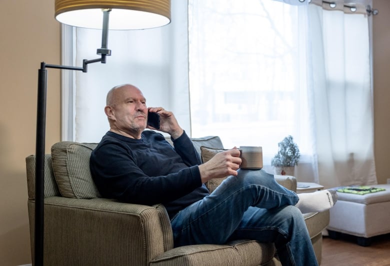 A man speaks on the phone while sitting in front of a window in a home. 