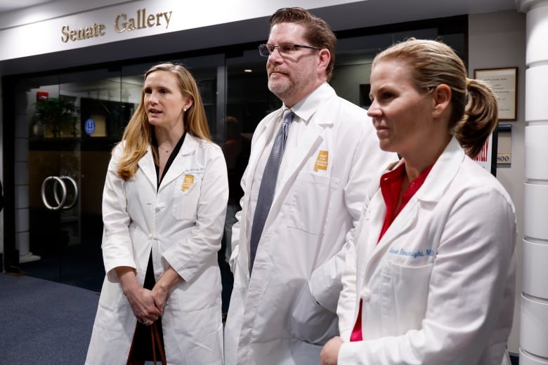 A man is flanked by two women, with all of them wearing medical coats.