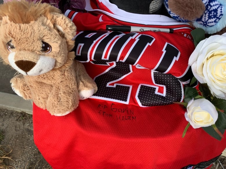 A pile of stuffed animals, a Chicago Bulls jerey and flowers sit on a lampost in a parking lot. 