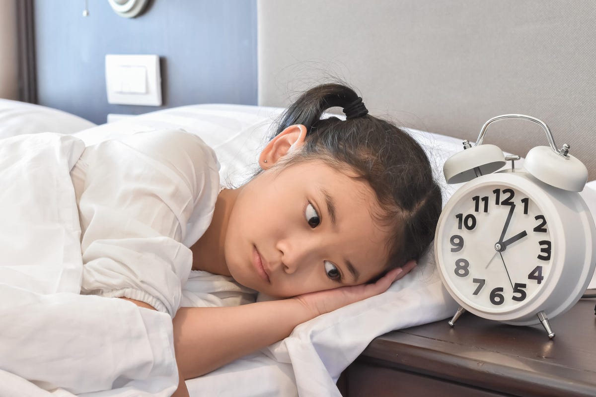 Little girl looking at an alarm clock with a sad face.