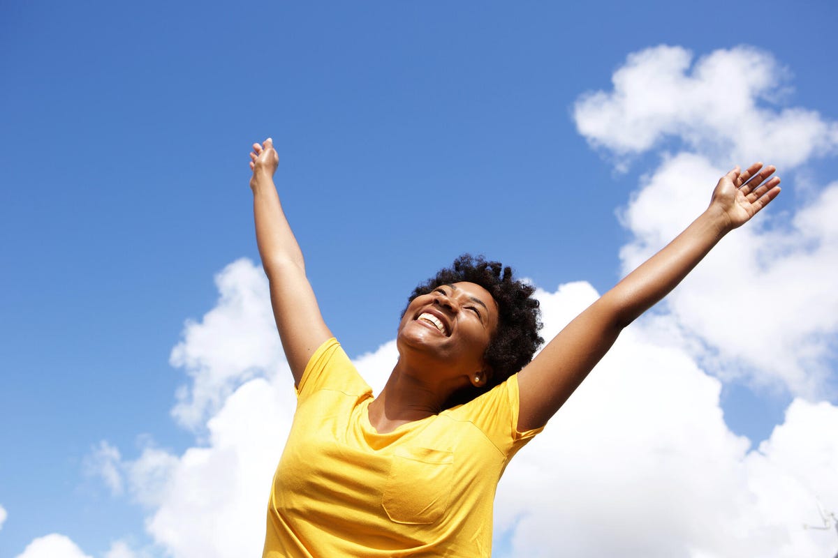 A happy woman in a yellow T-shirt throws up her arms