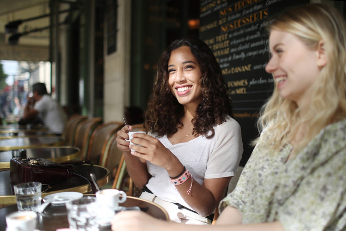 Two young women sitting on a patio, drinking coffee and laughing.