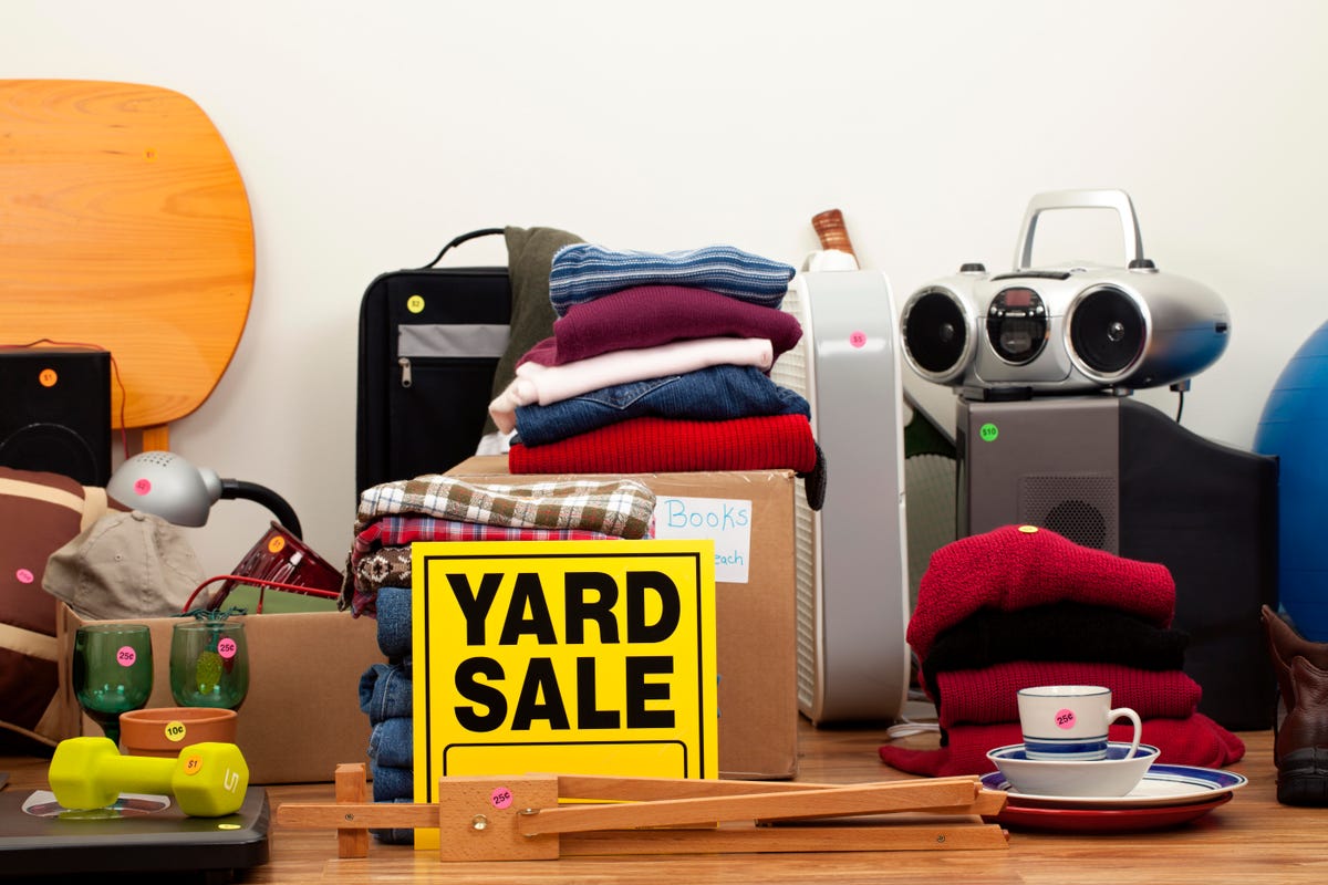 Piles of clothes and junk with a yard sale sign in front of it all.