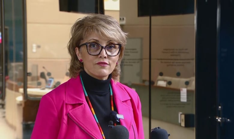 A woman in a pink blazer talks to reporters.