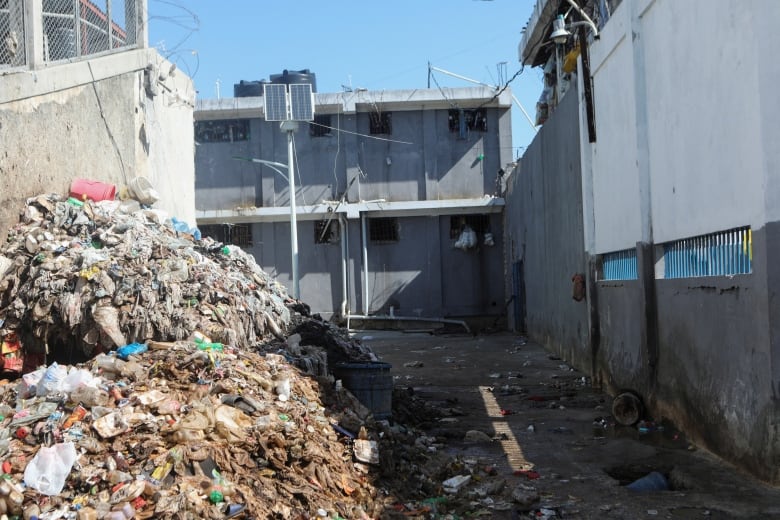 Piles of garbage and debris are shown in the alleway toward a building.