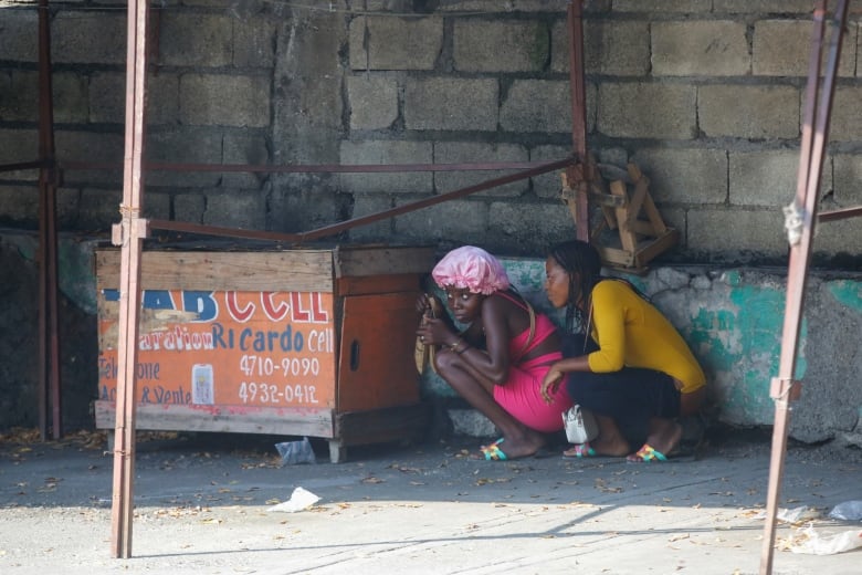 Two women crouch down in a covered area in an urban setting.