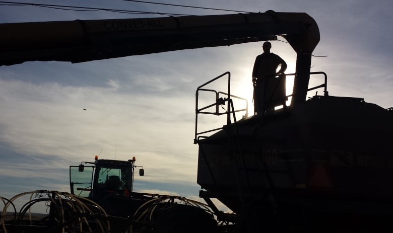 A silhouette shot of a farmer filling a seeder.