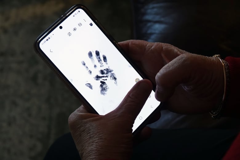 A black ink hand print on a phone screen. A woman is holding the phone.