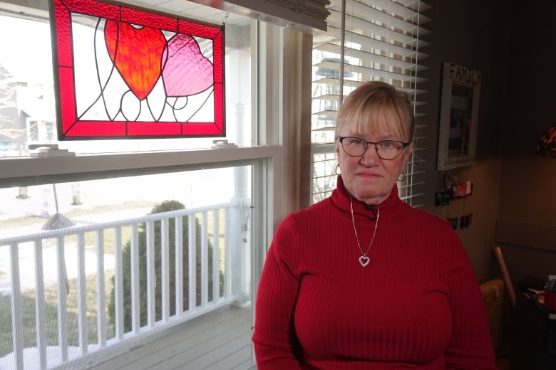 A woman in a red turtle neck stands next to a large window. A stained-glassed art piece spells out the word "love" below a pink and red heart.