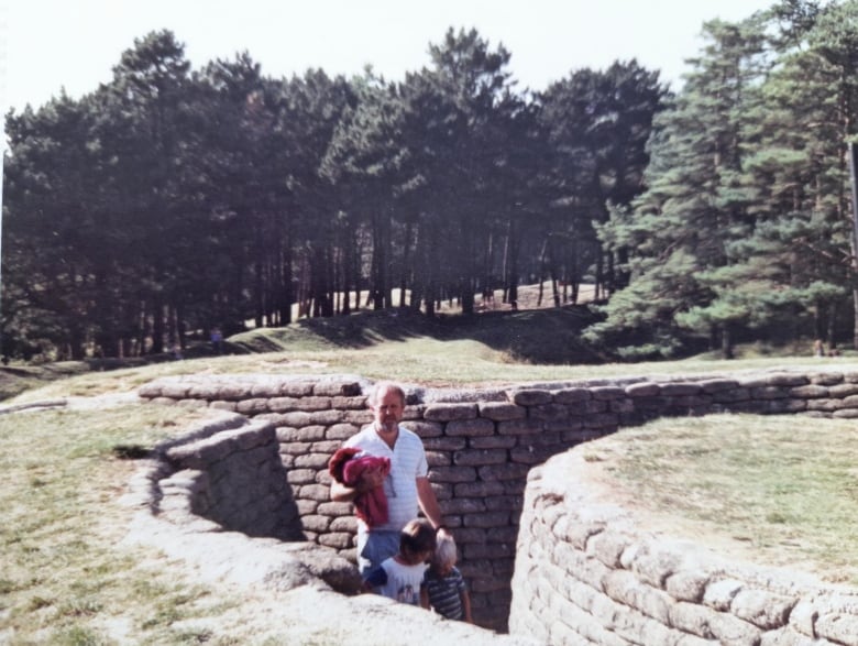 A weathered photo shows a man and two young boys standing in preserved trenches in France.