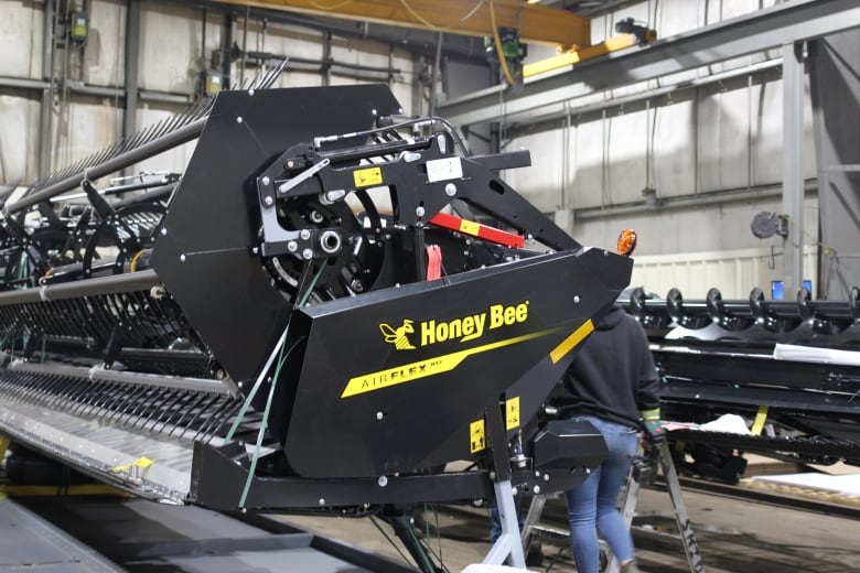 A black header with a yellow logo that says "Honey Bee" is pictured in a manufacturing facility as employees work in the background.