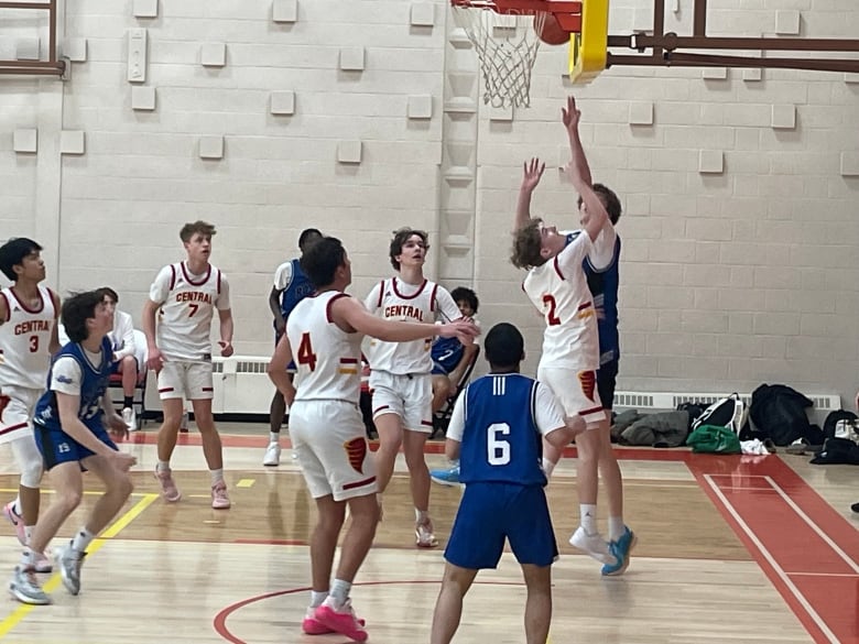 boys in white jerseys and blue jersey battle over a ball on a basketball court