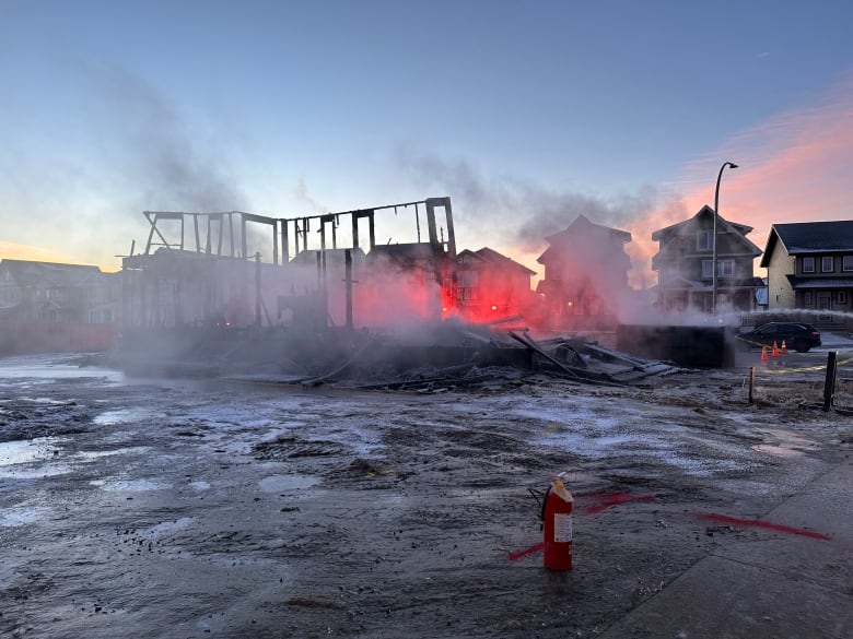 The framing of a house exposed by fire. The sun rises from the structure. Smoke rises from the exposed framing. 