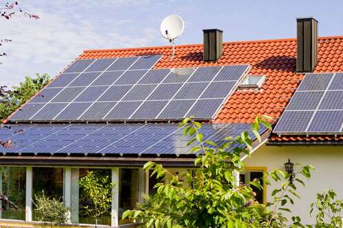 a white house with a Spanish tile roof and several solar panels