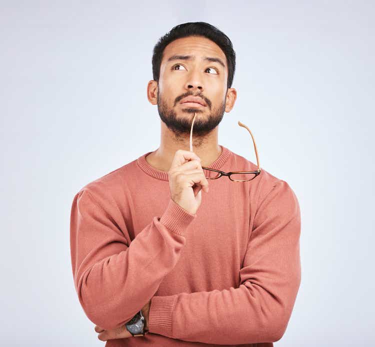 Decision, thinking and asian man in studio with glasses, questions and brainstorming on grey background. Why, idea and male person with emoji, body language or choice gesture, puzzled or solution