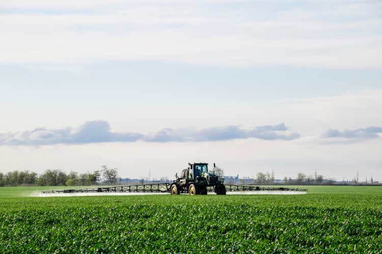 Tractor with a spray device for finely dispersed fertilizer. Tractor on the sunset background. Tractor with high wheels is making fertilizer on young wheat. The use of finely dispersed spray chemicals