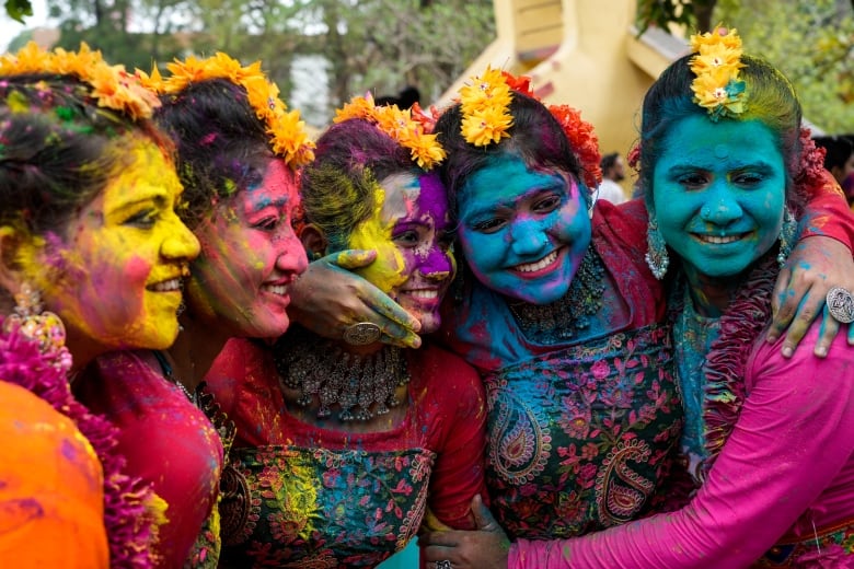 Five women with their faces smeared various colours, including yellow, purple and teal.