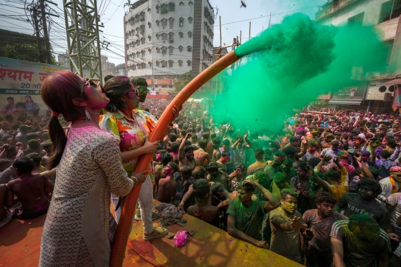 Women spray green powder from a hose on to a crowd of people.