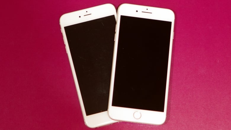 Two iPhones are set down on a pink-coloured surface.