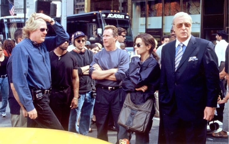 A group of actors and crew stand around mid-conversation on a city street.