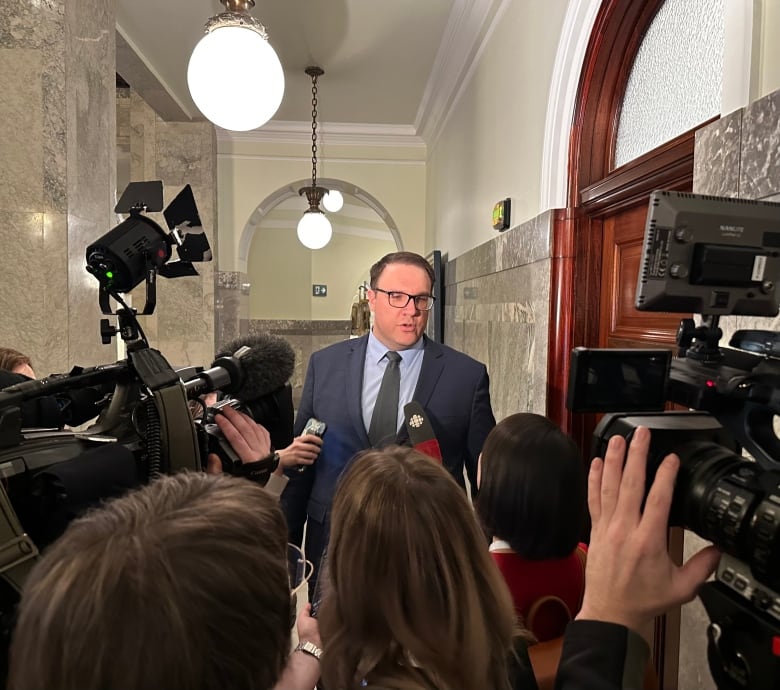 A man in a blue blazer answers questions from CBC News in front of TV cameras.