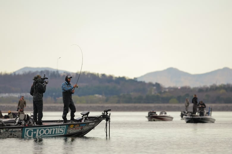 A man stands on a boat and casts a line into the water. 