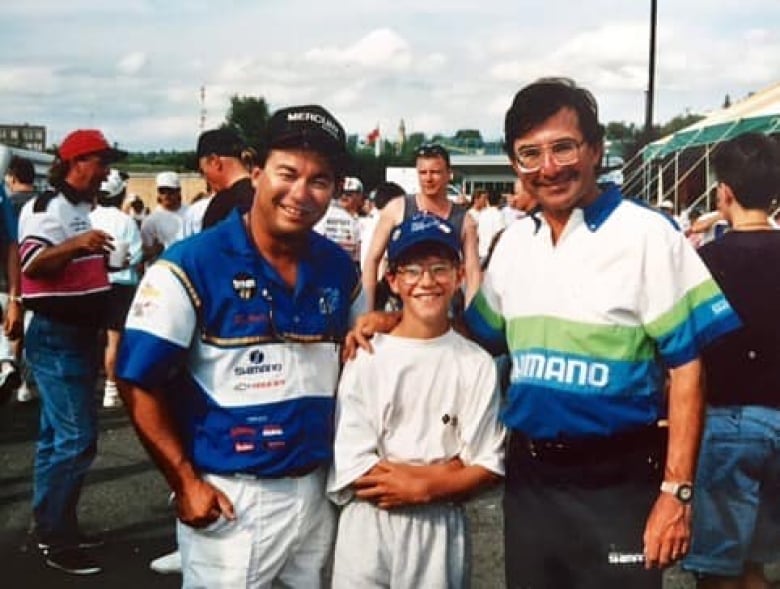 A young boy poses for a photograph with 2 older men standing next to him. 